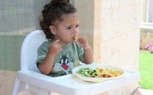 a child in a high chair eating more vegetables